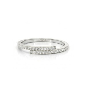 May include: A silver ring with a distinctive open design. The ring has a band of small, sparkling stones. The word "FIOR" is engraved on the band. The ring is set against a white background. A modern piece of jewellery.
