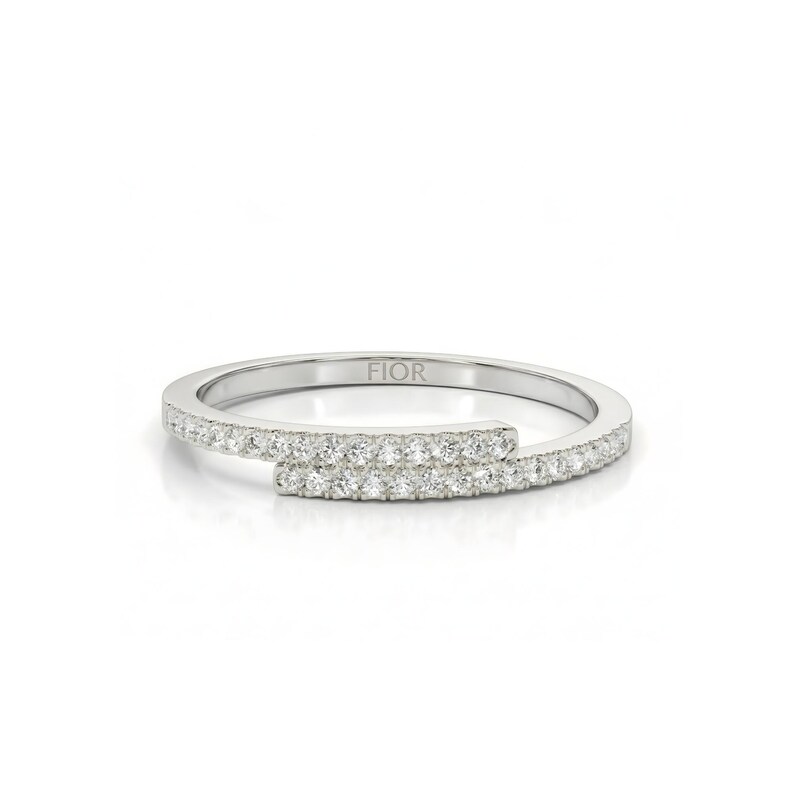 May include: A silver ring with a distinctive open design. The ring has a band of small, sparkling stones. The word "FIOR" is engraved on the band. The ring is set against a white background. A modern piece of jewellery.