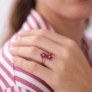 Puede incluir: Un anillo de oro con dos motivos en forma de flor, cada uno compuesto por cinco rub&iacute;es de color rosa intenso en talla marquesa que rodean un peque&ntilde;o diamante blanco central. El aro es fino y pulido, con los dos elementos florales juntos.