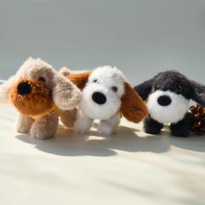 May include: Three soft toy dogs with floppy ears and black button eyes. One is tan and brown, another is white and brown, and the third is black and white. The toys are designed to be cuddly and are arranged in a row.