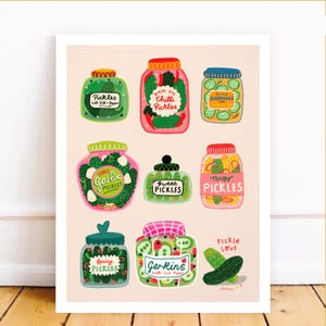 Può includere: Una stampa colorata con nove barattoli illustrati di sottaceti, ognuno con un'etichetta e un design unici. I barattoli sono riempiti con vari tipi di sottaceti, tra cui aneto, peperoncino e cetriolini. È presente anche la scritta "Pickle Love".