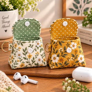 May include: Two small fabric pouches with snap closures and gold-tone metal rings. One pouch is cream with a green and yellow floral print and a green polka-dot interior. The other is yellow with a white floral print and a yellow polka-dot interior.