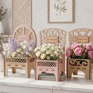 Può includere: Tre fioriere decorative in legno a forma di sedia da giardino, ognuna con fiori. Le fioriere sono rosa chiaro e legno naturale, con le parole "Bloom & Grow" e "Garden Chair Planter". I fiori sono bianchi, rosa e viola.