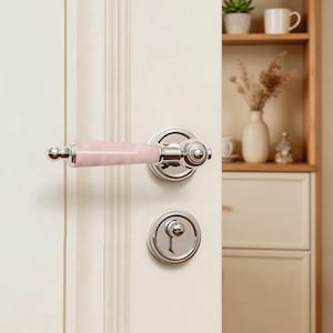 May include: A door handle set with a polished chrome finish and a pink, marbled-look handle. The set includes a matching door knob and keyhole, all mounted on a white door. The handle is approximately 6 inches long.