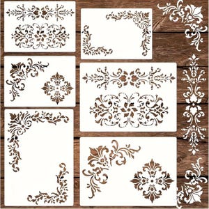 May include: A selection of white stencils featuring brown floral and ornamental designs. The stencils showcase corner, border, and medallion patterns, suitable for decorative painting and craft projects. The stencils are displayed on a wooden surface.