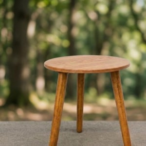 Puede incluir: Un pequeño taburete redondo de madera clara con tres patas. El taburete tiene un diseño sencillo y minimalista. Las patas están inclinadas hacia afuera para mayor estabilidad. Adecuado como mesa auxiliar o soporte para plantas.