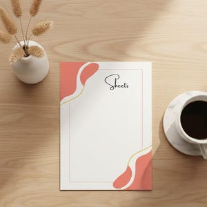 Könnte beinhalten: Ein weißes Blatt Papier mit dem Wort "Sheets" in Schreibschrift, mit korallenfarbenen und goldenen abstrakten Designs. Eine weiße Vase mit getrockneten Pflanzen und eine Tasse Kaffee auf einem Untersetzer aus Marmor sind ebenfalls zu sehen.