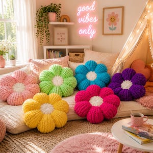 May include: A collection of six plush, flower-shaped pillows in vibrant colors including pink, lime green, yellow, bright blue, magenta, and purple. Each pillow features a soft, textured knit surface with a round, white, tufted center.