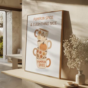 May include: A framed wall art print featuring a vertical stack of four ceramic mugs with autumn-themed illustrations. The text PUMPKIN SPICE & EVERYTHING NICE is printed at the top, and the bottom mug features the text PUMPKIN SPICE in orange.