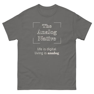 May include: A gray t-shirt with the text "The Analog Native" inside a white rectangular frame. Below the frame, the text "life is digital living is analog" is printed in white. The shirt is made of a soft material.