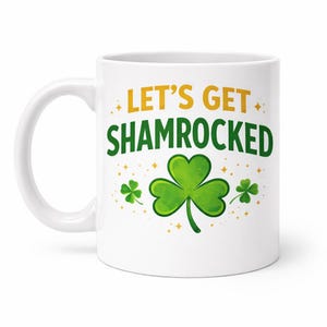 Puede incluir: Taza de cerámica blanca con el texto "LET'S GET SHAMROCKED" en verde y amarillo. La taza presenta un gran trébol verde y tréboles más pequeños con detalles de estrellas doradas, perfecta para el Día de San Patricio.