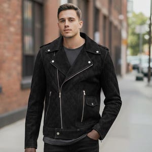 Könnte beinhalten: Schwarze, gesteppte Lederjacke mit diagonalem Reißverschluss, zwei Vordertaschen und silberfarbenen Details. Die Jacke hat einen klassischen Biker-Stil mit Reverskragen und Schulterklappen. Das Model trägt ein graues T-Shirt und eine schwarze Jeans.