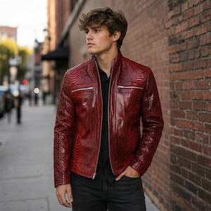 May include: A deep red jacket with a textured snakeskin pattern, featuring a stand-up collar, a full-length front zipper, and two horizontal zippered chest pockets. The jacket is worn over a black button-down shirt and dark gray denim jeans.