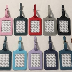 Può includere: Una collezione di dieci etichette per bagagli in vari colori, tra cui rosa, verde, rosso, grigio e nero. Ogni etichetta ha una finestra rettangolare con un supporto bianco e un cinturino con fibbia. Le etichette sono in similpelle.