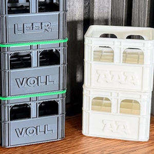 Könnte beinhalten: Eine weiße Keramik-Tasse mit schwarzem Henkel und dem Text "But First, Coffee" in fetter, schwarzer Schrift. Die Tasse steht vor einem verschwommenen Hintergrund, der eine gemütliche Umgebung suggeriert.