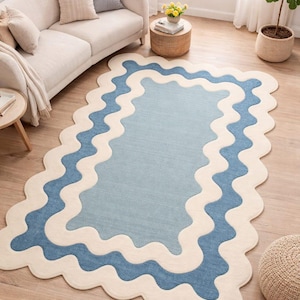 Peut inclure: Un tapis bleu clair et crème avec une bordure ondulée. Le tapis a une forme rectangulaire avec un centre bleu clair et une bordure crème. Le tapis est posé sur un parquet dans un salon.