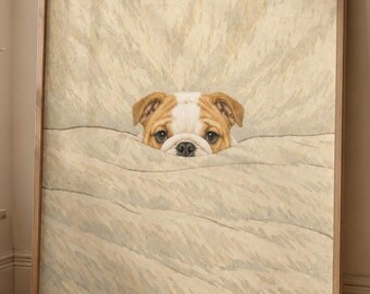 Puede incluir: Impresión enmarcada que presenta un bulldog asomando por encima de una manta beige texturizada. El perro tiene un pelaje blanco y marrón. El marco es de color marrón claro. La obra se exhibe contra una pared neutra.