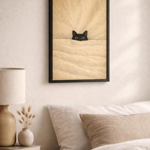 Puede incluir: L&aacute;mina enmarcada que muestra un gato negro asomando por encima de una manta beige. Se ven los ojos del gato, a&ntilde;adiendo un toque de fantas&iacute;a. La obra est&aacute; enmarcada en negro, ideal para la decoraci&oacute;n de dormitorios o salones.