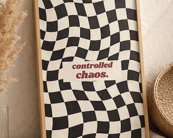 Puede incluir: Una impresión artística enmarcada con un patrón de cuadros en blanco y negro que parece ondulado. Las palabras "controlled chaos." están impresas en color burdeos en el centro. El marco es de color marrón claro.