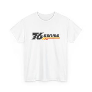 Puede incluir: Camiseta blanca con el texto "76 SERIES" en negro, amarillo y rojo. El diseño incluye el número estilizado 76 y rayas horizontales. La camiseta está hecha de un material suave y cómodo.