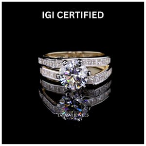 Pode incluir: Um anel de diamante com uma grande pedra central redonda e uma banda adornada com diamantes menores de corte retangular. O anel é apresentado sobre um fundo preto, com o texto "IGI CERTIFIED" no topo e "TAPASVI JEWELS" na parte inferior.