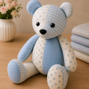 May include: A stuffed teddy bear crafted from various light blue and white fabrics featuring patterns of small flowers, polka dots, and gingham checks. The bear has two round black eyes and a black nose, with a seated posture and stitched seams.