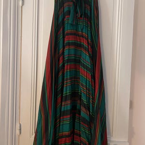 May include: A long, flowing skirt with a vibrant striped pattern in shades of green, red, and black. The skirt features a tie-waist design and hangs from a black hanger. The fabric appears lightweight and suitable for warmer weather.