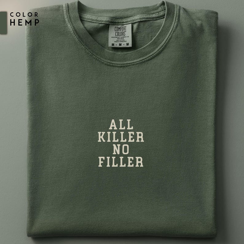 May include: A folded, olive green t-shirt with the text "ALL KILLER NO FILLER" in white block letters. The shirt has a crew neck and short sleeves. The brand tag is visible at the neckline.