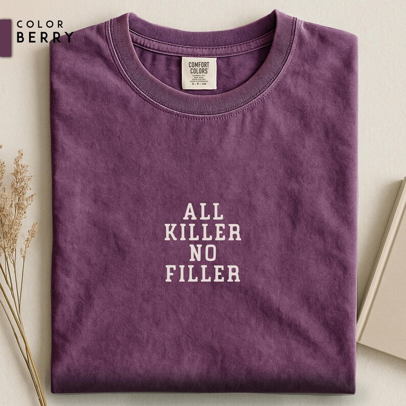 May include: Berry-colored t-shirt with the text "ALL KILLER NO FILLER" in white block letters. The shirt is folded neatly, showcasing the crew neck and the Comfort Colors label. The color swatch "BERRY" is in the upper left corner.