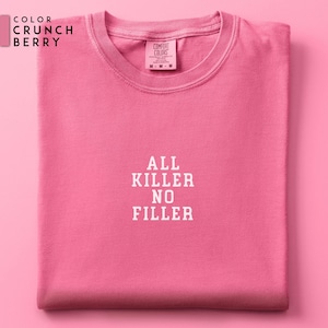 May include: A folded, short-sleeved, crew neck t-shirt in a vibrant Crunch Berry pink. The shirt features the text "ALL KILLER NO FILLER" in white block letters. The Comfort Colors brand tag is visible at the neckline.