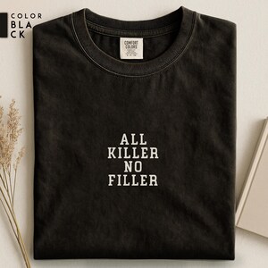 May include: Black t-shirt with the text "ALL KILLER NO FILLER" in white block letters. The shirt has a crew neck and a tag that reads "COMFORT COLORS". The color of the shirt is black.