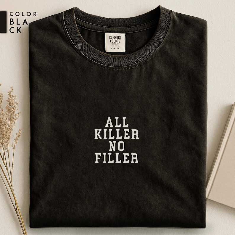 May include: Black t-shirt with the text "ALL KILLER NO FILLER" in white block letters. The shirt has a crew neck and a tag that reads "COMFORT COLORS". The color of the shirt is black.