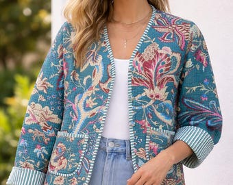 Puede incluir: Una chaqueta acolchada de color verde azulado con un estampado floral en tonos rosa, crema y azul. La prenda cuenta con mangas tres cuartos con puños a rayas, cuello redondo y dos bolsillos delanteros con ribetes a rayas.