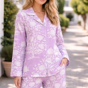 May include: Lilac pyjama set featuring a white floral design. The set comprises a button-down shirt with white piping and matching trousers. The sleepwear is made from a soft material, suitable for a comfortable night's sleep.