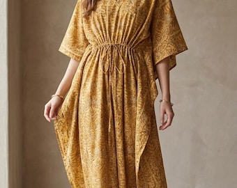 Puede incluir: Un vestido caftán de color amarillo mostaza con escote en V, mangas anchas estilo kimono y cintura con cordón ajustable. La prenda está decorada con un intrincado patrón floral tonal repetitivo y llega a media pantorrilla con aberturas laterales.