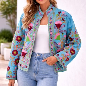 May include: A light blue embroidered jacket with a mandarin collar and long sleeves. The jacket is decorated with pink, red, and green floral embroidery. The model is wearing a white top and blue jeans. The jacket is a stylish outerwear item.