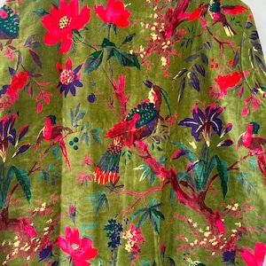 Op de afbeelding: Een jas met lange mouwen van olijfgroen fluweel met een levendige botanische print. Het patroon toont diverse kleurrijke vogels op takken, afgewisseld met felrode bloemen, paarse bloesems en gele florale accenten.