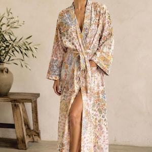 May include: A long-length robe featuring a multi-colored floral pattern in shades of pink, orange, blue, and yellow on a white background. The robe has long, wide sleeves, a V-neckline, and a matching fabric tie belt at the waist.