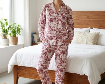 Puede incluir: Un conjunto de pijama de dos piezas que incluye una camisa de manga larga con botones y cuello, y pantalones largos a juego, ambos decorados con un estampado floral rojo oscuro sobre fondo blanco. La camisa tiene un bolsillo delantero.