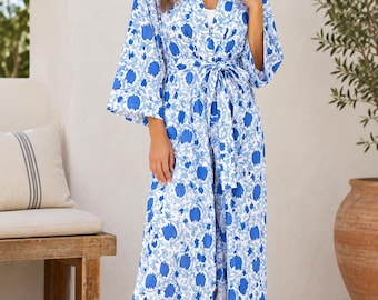 Puede incluir: Una bata larga hasta los pies con un estampado floral en azul y blanco. La prenda tiene mangas anchas de tres cuartos, un escote en V y un cinturón de tela a juego en la cintura para asegurar el cierre frontal.