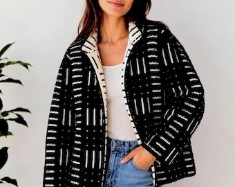 Puede incluir: Una chaqueta negra con un patrón geométrico blanco de líneas verticales y pequeños puntos. La chaqueta tiene un forro interior de color crema visible a lo largo de la abertura frontal y el cuello, sobre una camiseta blanca y pantalones vaqueros azules.
