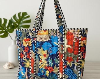 Puede incluir: Un bolso tote acolchado con un vibrante estampado floral en tonos azules, rojos, amarillos y verdes. El bolso tiene asas y ribetes a rayas blancas y negras. El bolso mide aproximadamente 38 cm de ancho y 30 cm de alto.