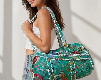 Puede incluir: Una bolsa de viaje cilíndrica con una base de color verde azulado vibrante y un estampado floral y de cachemira multicolor. La bolsa incluye correas de tela a rayas blancas y verde azuladas, una hebilla de metal dorado y costuras acolchadas.