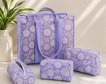 Puede incluir: Un bolso tote acolchado y tres estuches a juego en tela de color morado claro con un estampado floral blanco. El bolso tiene dos asas y un borde de cuadros azules y blancos. Los estuches son rectangulares, uno de ellos con cremallera blanca.