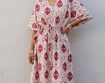 Puede incluir: Un vestido caftán largo hasta los pies con base blanca y un patrón repetitivo de rombos magenta que contiene ilustraciones de abejas y motivos florales pequeños. La prenda tiene cuello en V, mangas tipo kimono y cordón ajustable.