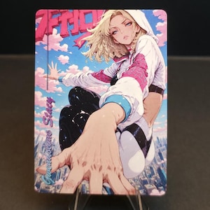 May include: A trading card featuring an anime-style illustration of a blonde woman in a white hoodie with pink and blue accents. The card has the word "ACTION" in pink and the name "Gwen Stacy" in cursive.