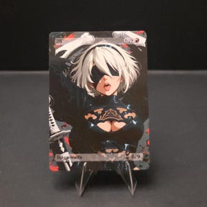 May include: A trading card featuring a character with white hair, a black blindfold, and a black outfit. The card has the text "Token Waifu" and "6/9". The background is dark with red accents.