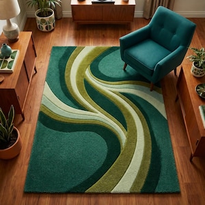 Könnte beinhalten: Ein teal- und grün gemusterter Teppich mit einem fließenden, abstrakten Design. Der Teppich weist eine Mischung aus teal, olivgrünen und cremefarbenen, geschwungenen Streifen auf, die ein strukturiertes, wellenartiges Muster erzeugen. Der Teppich liegt auf einem Holzboden, mit einem tealfarbenen Sessel und Holzmöbeln im Hintergrund.