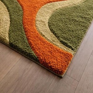 Abstract wave shaggy rug in olive green, orange, and cream colors placed in a modern living room with beige sofa and large windows