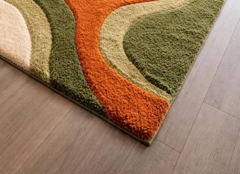 Abstract wave shaggy rug in olive green, orange, and cream colors placed in a modern living room with beige sofa and large windows